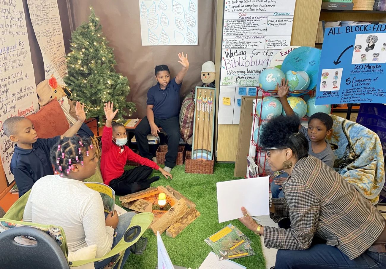 kids raising their hand while listening to an adult read a story