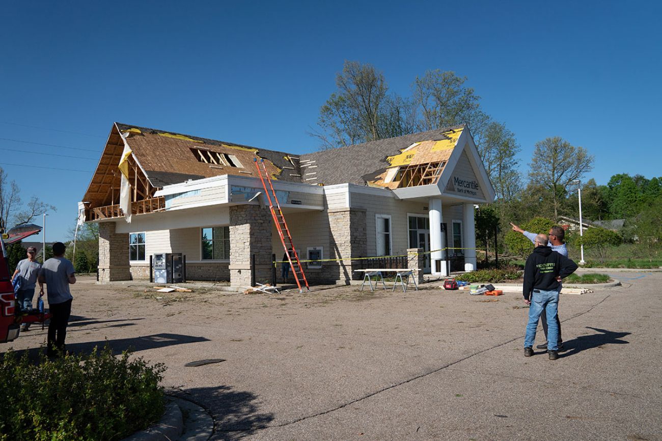 patches of the roof are missing. People are outside, looking at the building