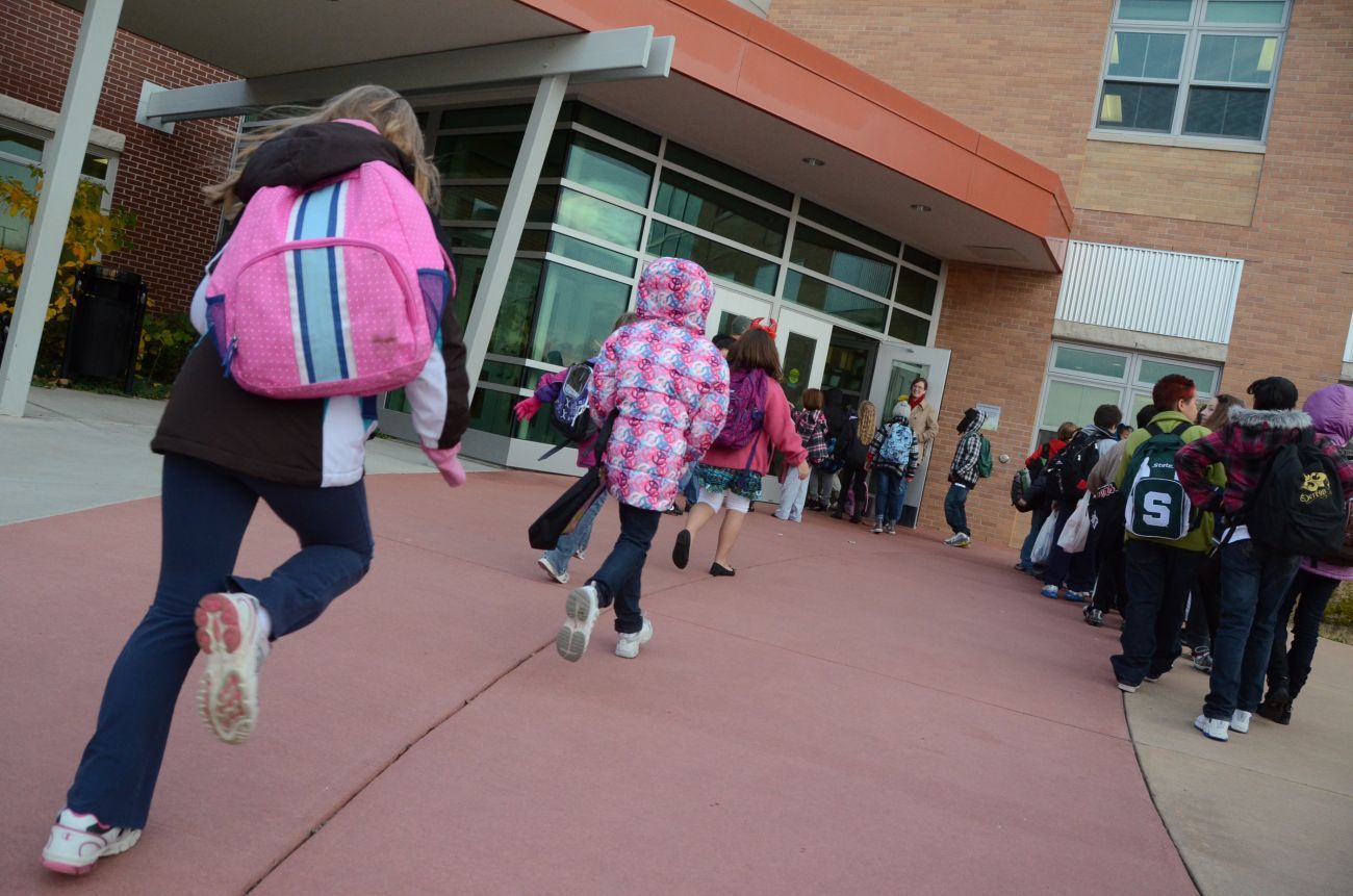 Children with backpacks running in front of a school