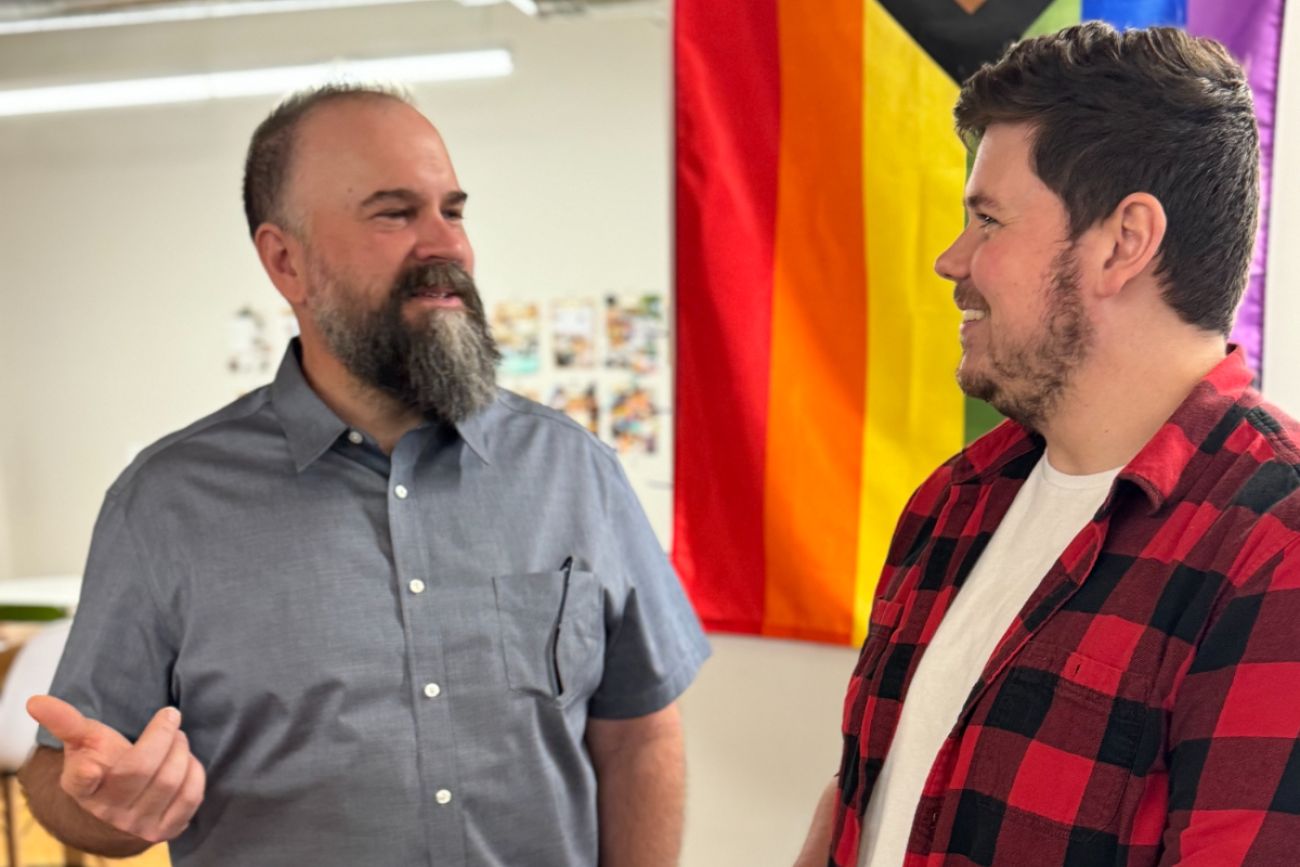 Two people talking to each other. One is wearing a grey shirt and the other is wearing a red fannel