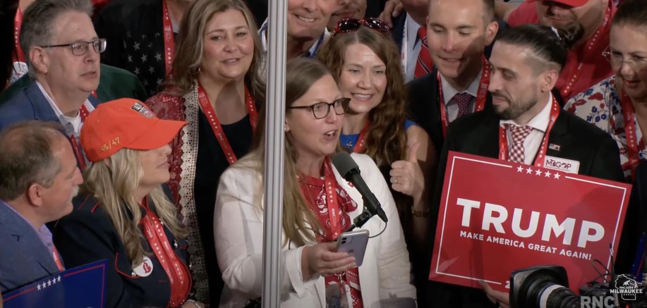 A bunch of people standing; one person holding a Trump sign