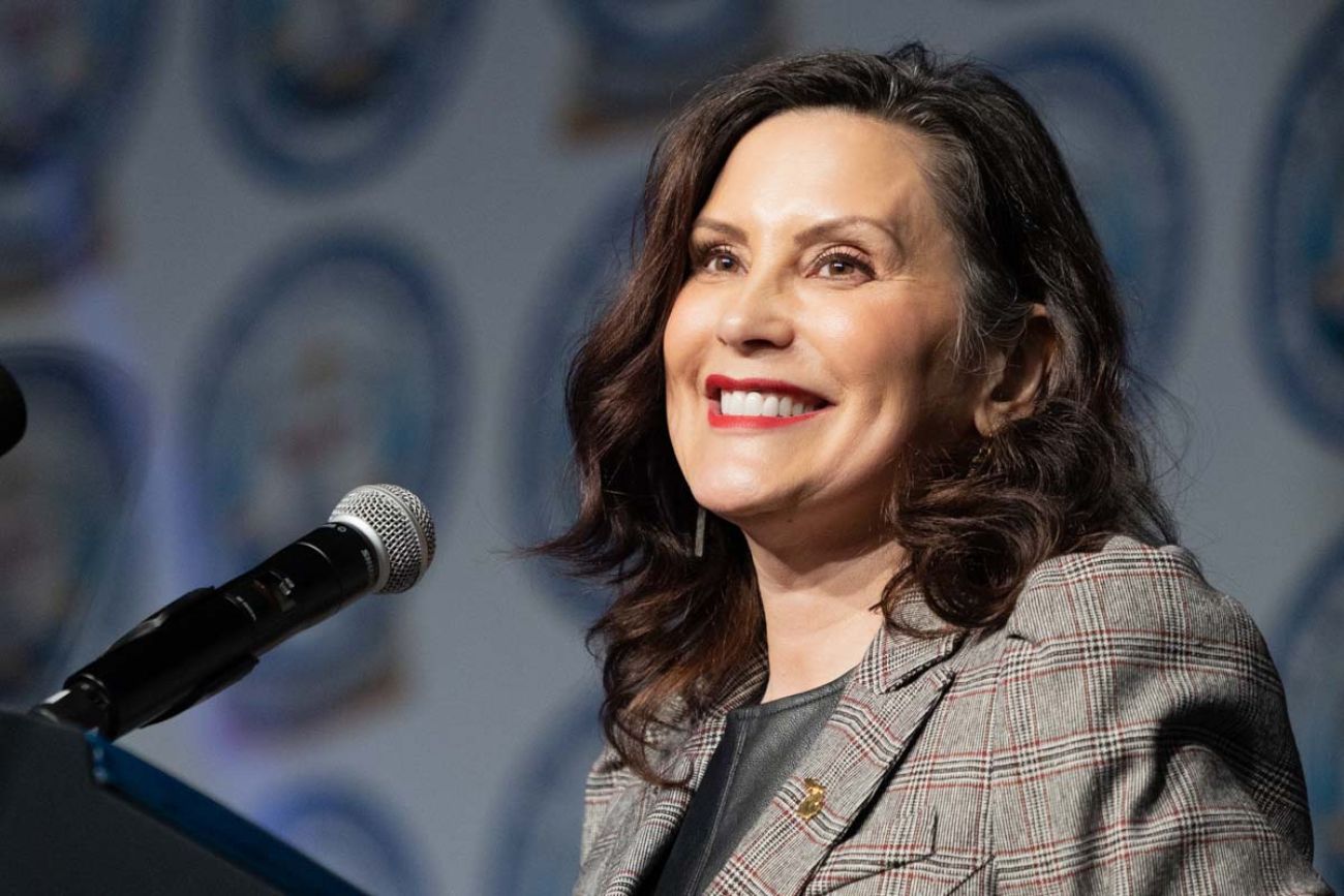 Michigan Gov. Gretchen Whitmer, wearing a grey jacket, speaks into a microphone