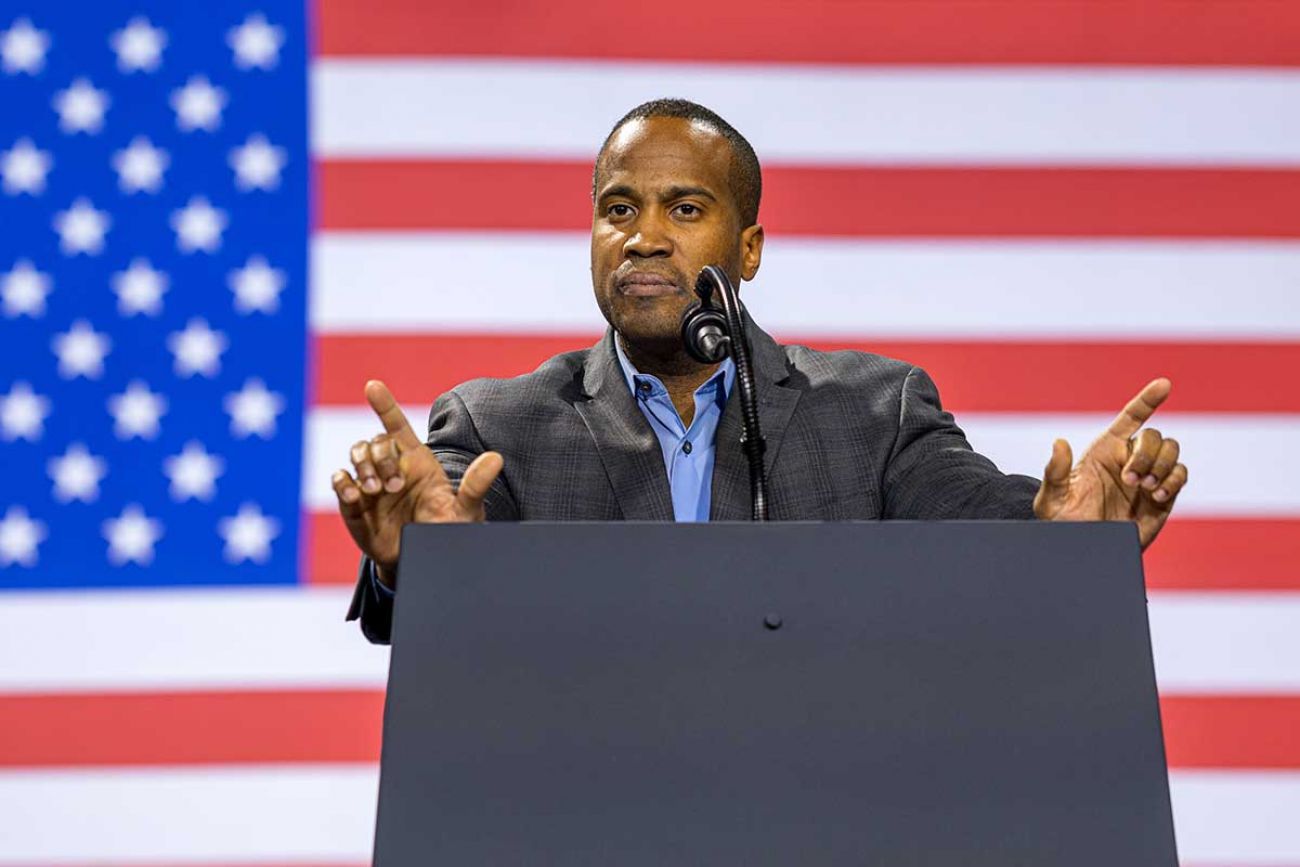 John James on a stage; US flag in the background