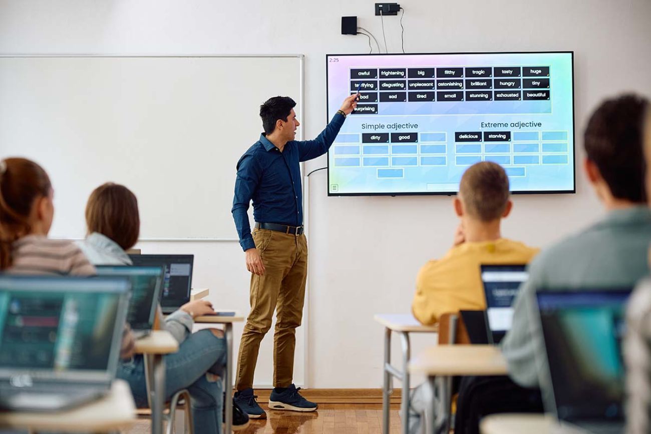 Male teacher using interactive whiteboard while giving a lesson to high school students in the classroom.