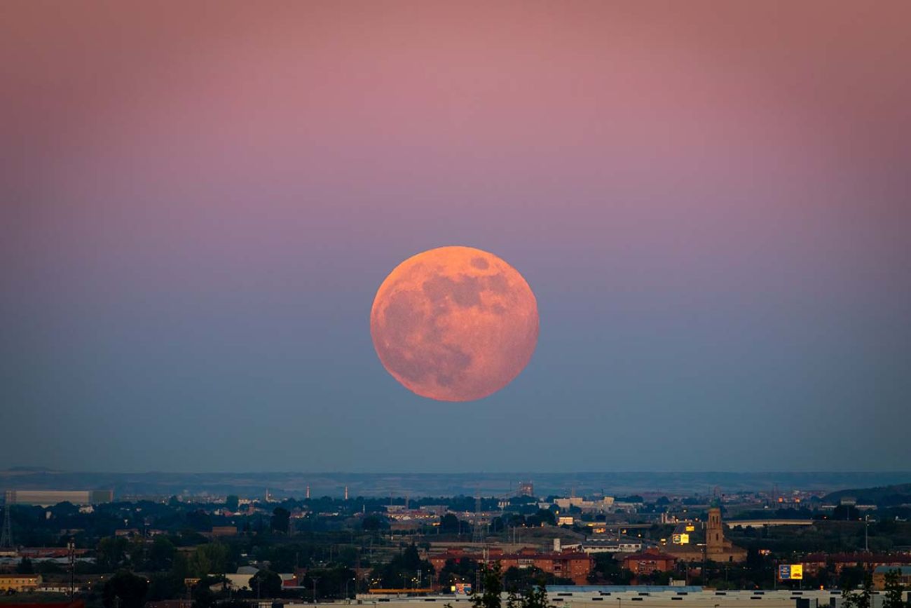 The strawberry Supermoon at sunset gradient from blue to pink on the city skyline in June 2020 in Spain.