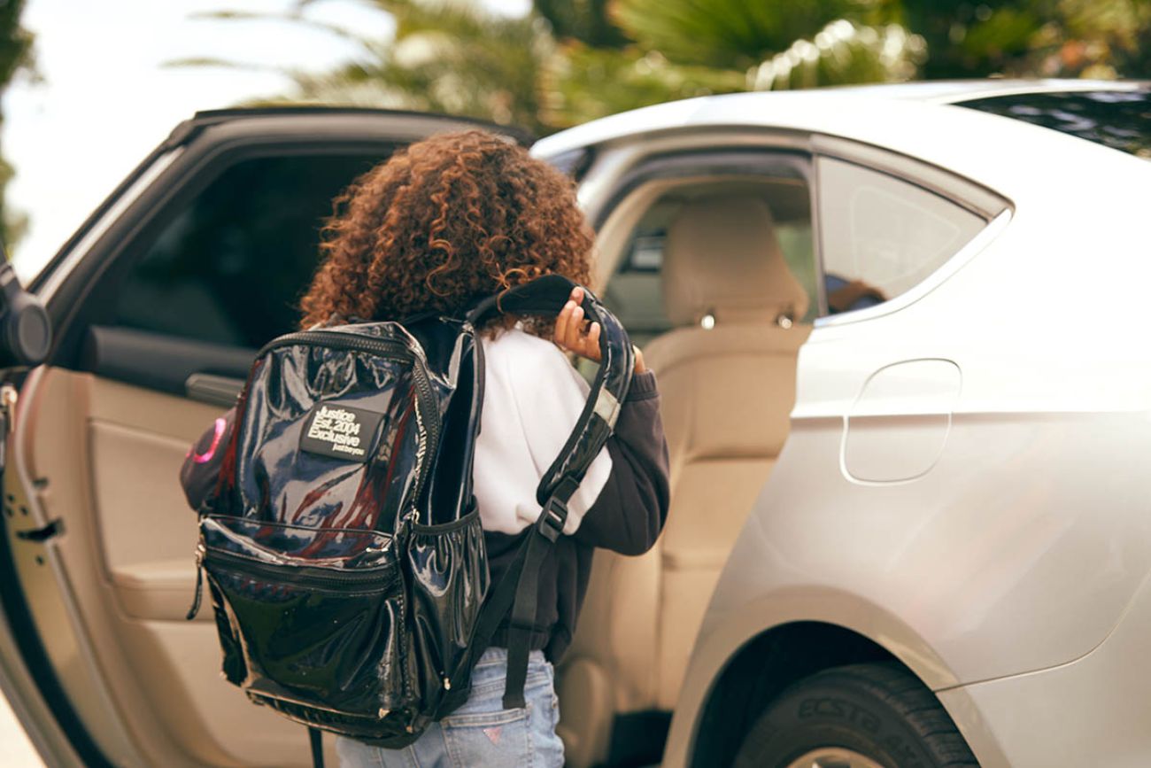 A girl with a backpack goes into a white car