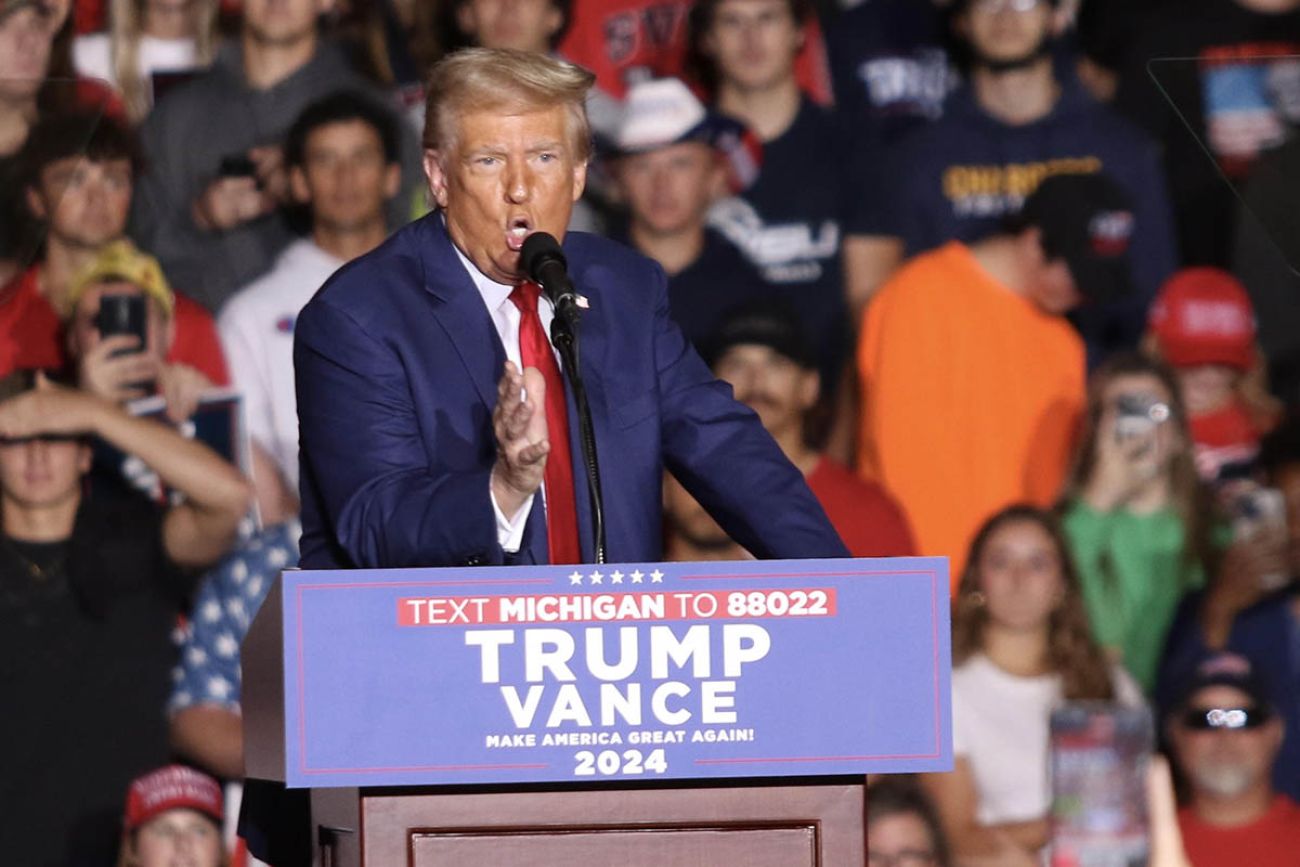 Donald Trump on stage; supporters are cheering behind him