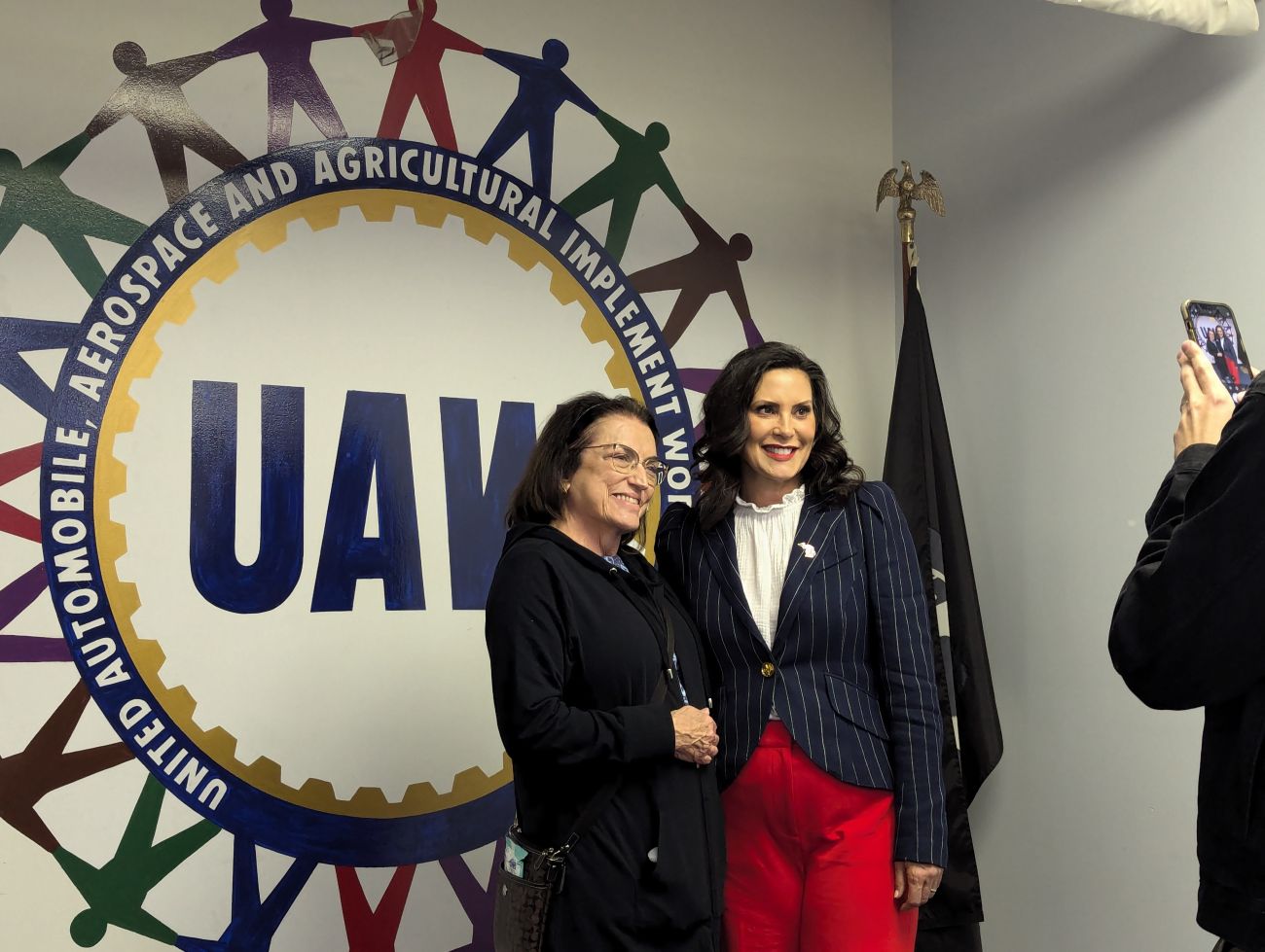 Gov. Gretchen Whitmer stands next to a woman in front of the UAW logo on a wall