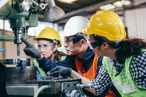 male foreman manager showing case study of factory machine to two engineer trainee