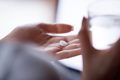 Close up woman holding pill in hand with water