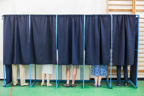 some people voting in at polling booth. They are covered by a black curtain but you can see their feet