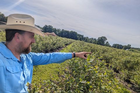 Chad Reenders is wearing a white cowboy hat and blue shirt. He is in a farm 