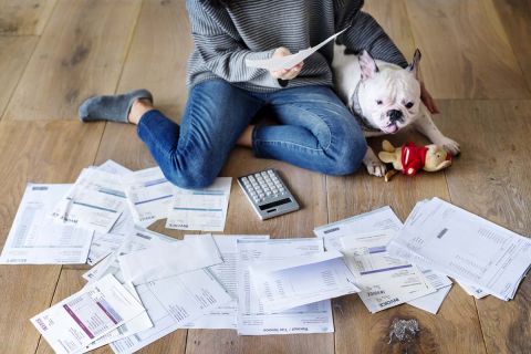 Woman sits on the floor with her white dog. Bills are on the floor