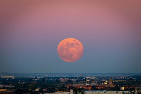 The strawberry Supermoon at sunset gradient from blue to pink on the city skyline in June 2020 in Spain.