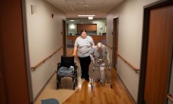 one woman walking next to a woman using a walker in a hallway