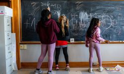 three kids in front of a blackboard. one of the kids is completing a math problem 