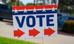 A VOTE sign at a polling place on green grass near a parking lot