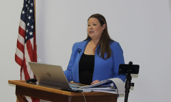 Stefanie Lambert, wearing a blue professional jacket, speaks into a podium