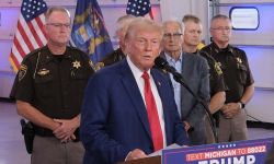 Donald Trump speaking into a microphone, law enforcement officers stand behind him