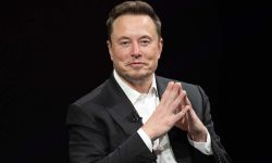 Elon Musk in a black suit, sitting in front of black background