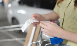  Close up of hand woman checking long grocery receipt bill after shopping at car park of supermarket